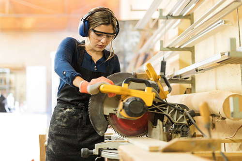 Woman cutting wood in a workshop